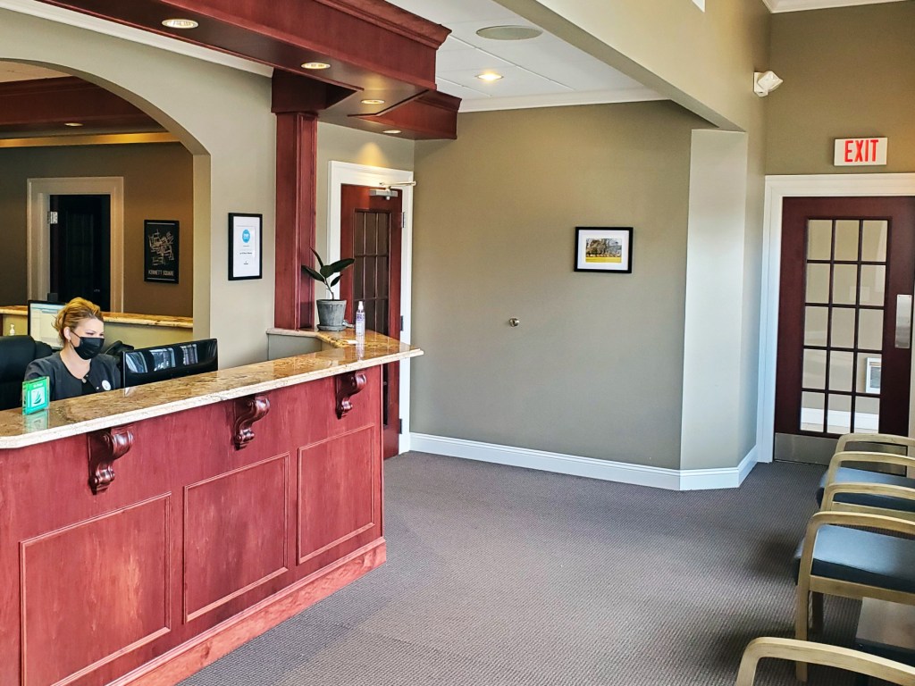 Waiting room chairs, front desk, and receptionist at {PRACTICE_NAME}